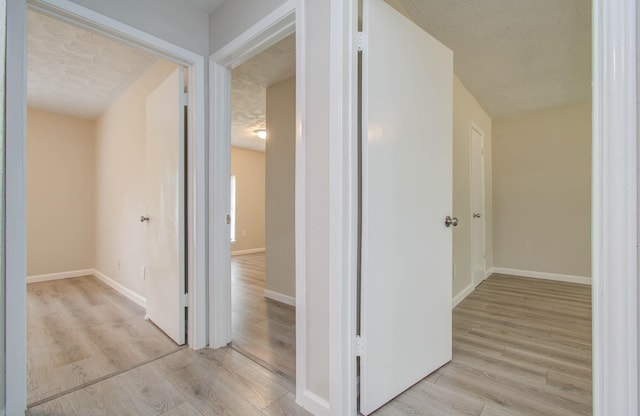 hall with a textured ceiling and light wood-type flooring