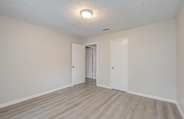 spare room featuring a textured ceiling and light hardwood / wood-style flooring