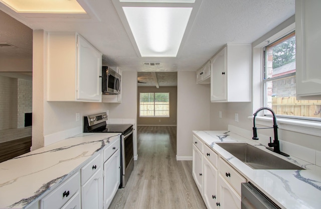 kitchen featuring white cabinetry, stainless steel appliances, light stone countertops, and sink