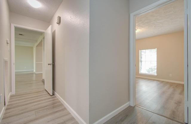 hallway with light hardwood / wood-style flooring and a textured ceiling