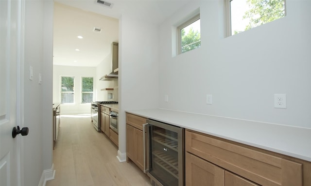 bar featuring appliances with stainless steel finishes, beverage cooler, light hardwood / wood-style floors, and wall chimney exhaust hood