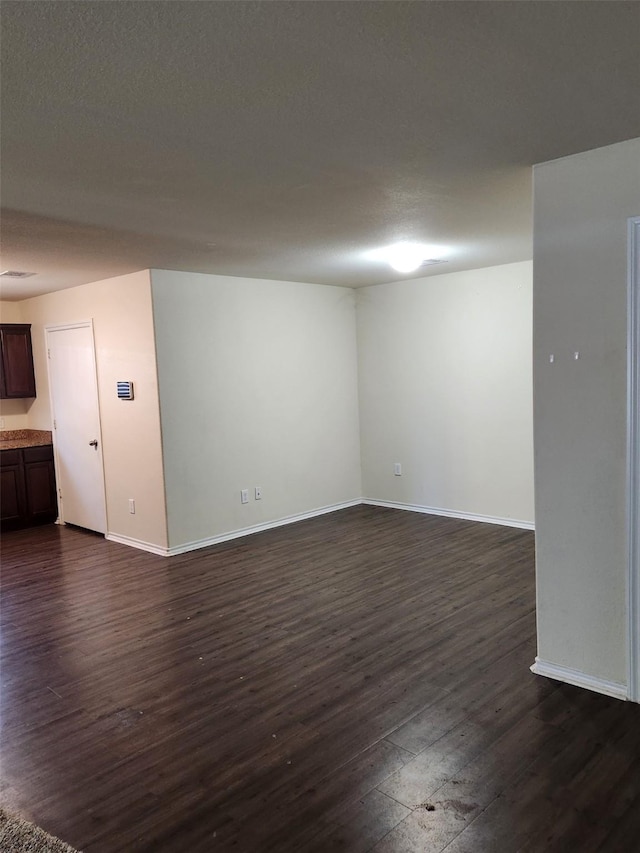 empty room with a textured ceiling, dark wood finished floors, and baseboards