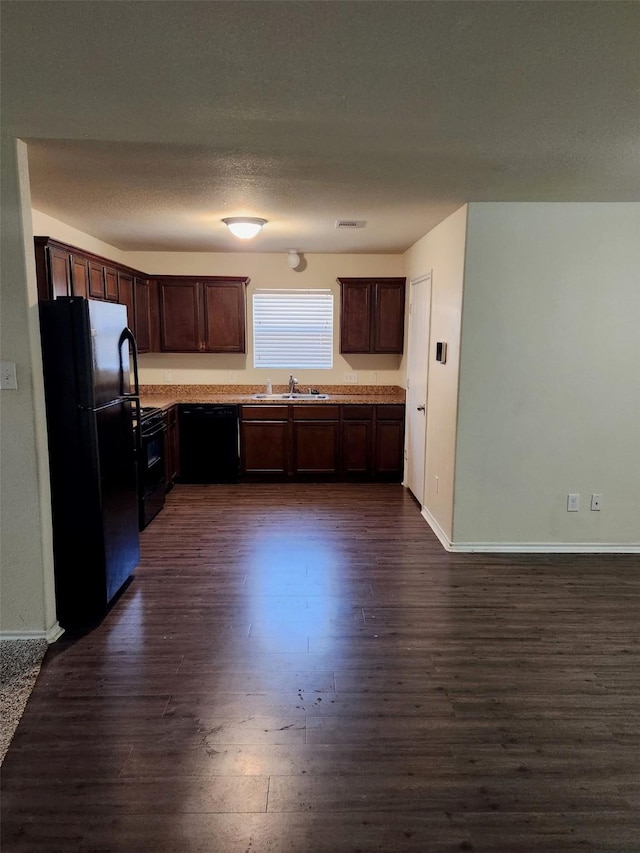 kitchen featuring dark wood finished floors, light countertops, dark brown cabinets, black appliances, and a sink