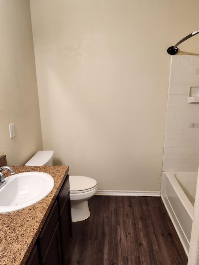 bathroom with toilet, wood finished floors, vanity, baseboards, and shower / washtub combination