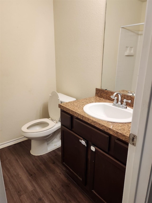 bathroom with toilet, wood finished floors, vanity, baseboards, and a shower