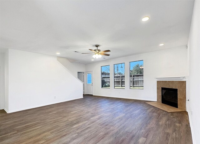 unfurnished living room featuring a tiled fireplace, dark wood-type flooring, and ceiling fan