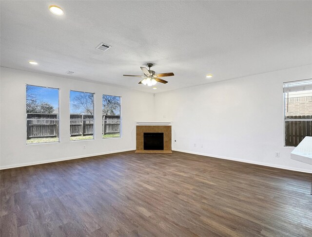 unfurnished living room featuring a textured ceiling, visible vents, baseboards, a tiled fireplace, and dark wood finished floors