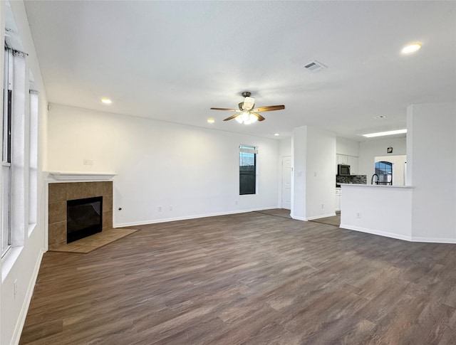 unfurnished living room with a fireplace, visible vents, dark wood-type flooring, a ceiling fan, and baseboards