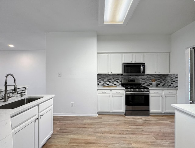 kitchen with white cabinets, stainless steel gas range oven, light countertops, and a sink