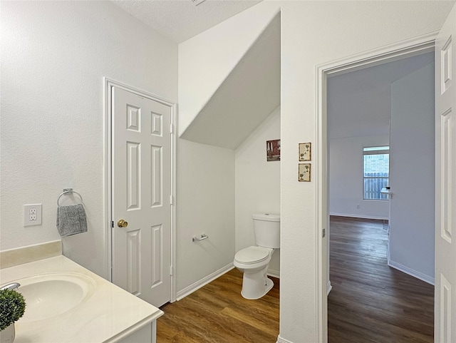 bathroom featuring lofted ceiling, toilet, vanity, wood finished floors, and baseboards