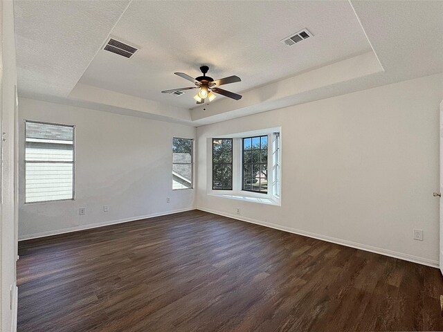 unfurnished room featuring a raised ceiling, plenty of natural light, dark wood-type flooring, and ceiling fan