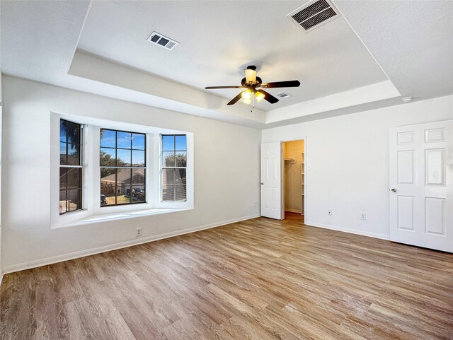 unfurnished bedroom featuring ceiling fan, a walk in closet, a raised ceiling, and light wood-type flooring