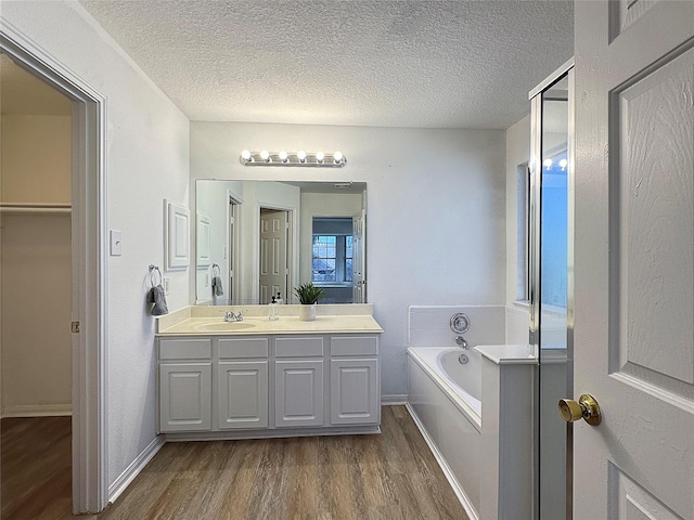 full bathroom with a garden tub, a textured ceiling, wood finished floors, and vanity