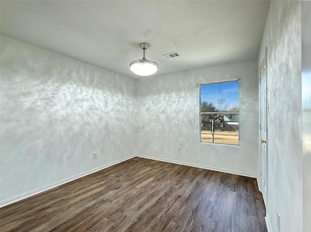 spare room featuring dark wood-style flooring, visible vents, and baseboards