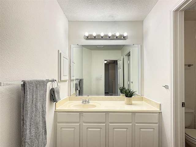 bathroom featuring toilet, a textured wall, a textured ceiling, and vanity