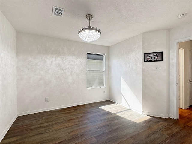 empty room featuring dark wood-style flooring, visible vents, a textured ceiling, and baseboards