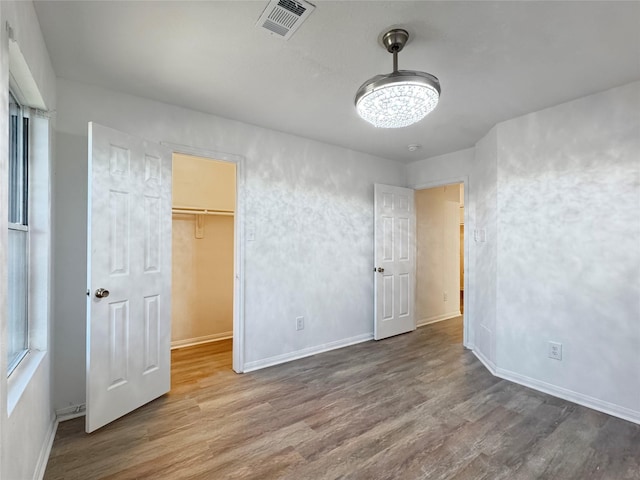 unfurnished bedroom featuring baseboards, visible vents, a walk in closet, and wood finished floors