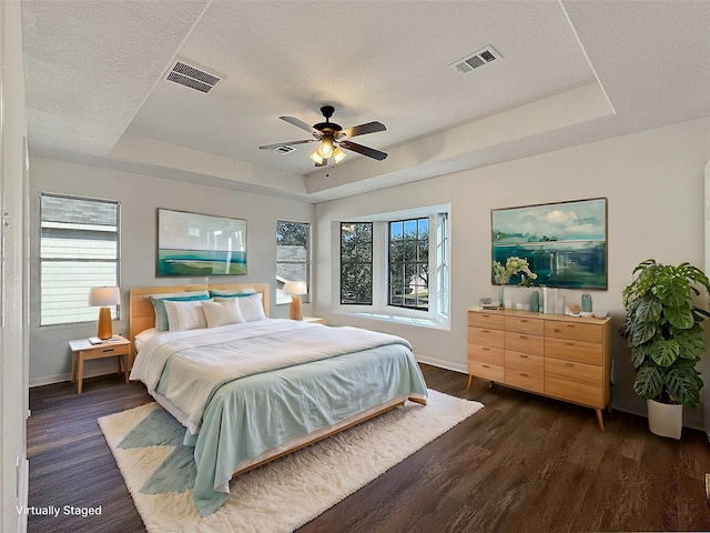 bedroom with dark wood-style floors, a raised ceiling, and visible vents