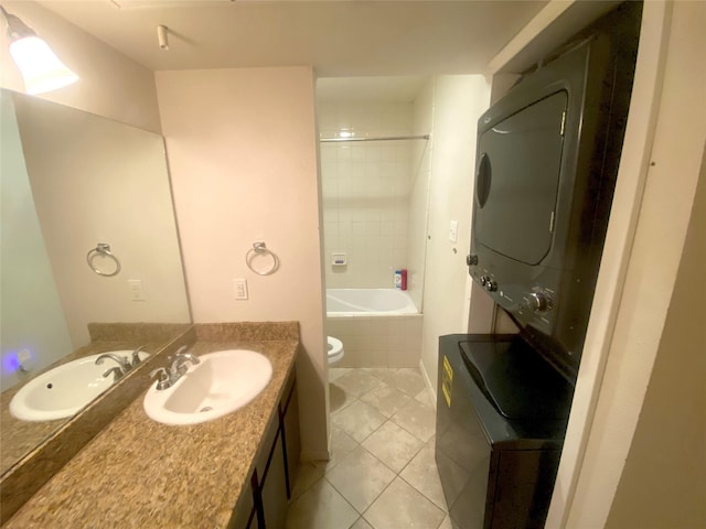 full bathroom featuring stacked washer / dryer, tiled shower / bath combo, vanity, tile patterned flooring, and toilet