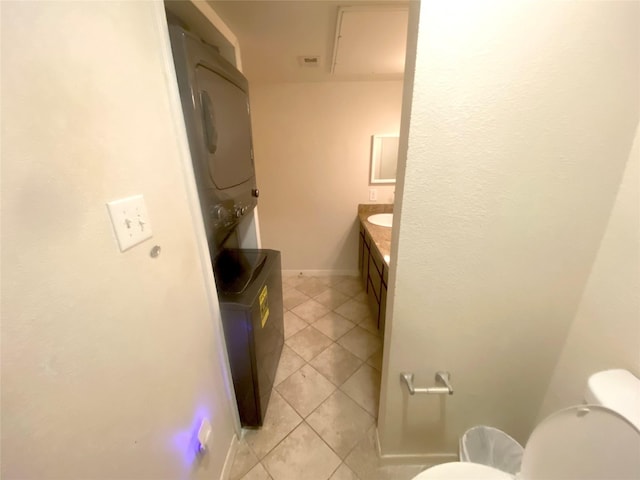 bathroom with stacked washer / dryer, vanity, toilet, and tile patterned flooring