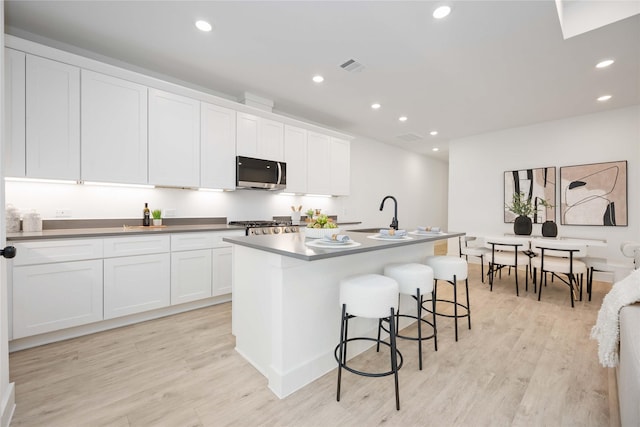 kitchen featuring sink, a center island with sink, white cabinets, and light wood-type flooring