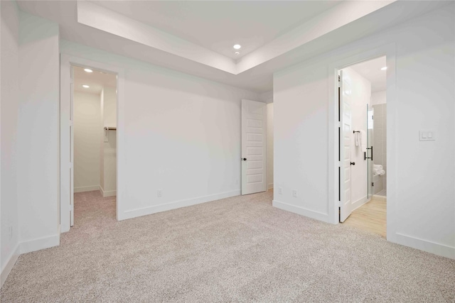 unfurnished bedroom featuring light colored carpet, a tray ceiling, ensuite bath, and a spacious closet