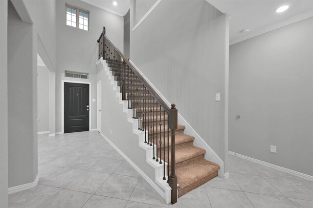 entryway featuring a towering ceiling, ornamental molding, and light tile patterned flooring