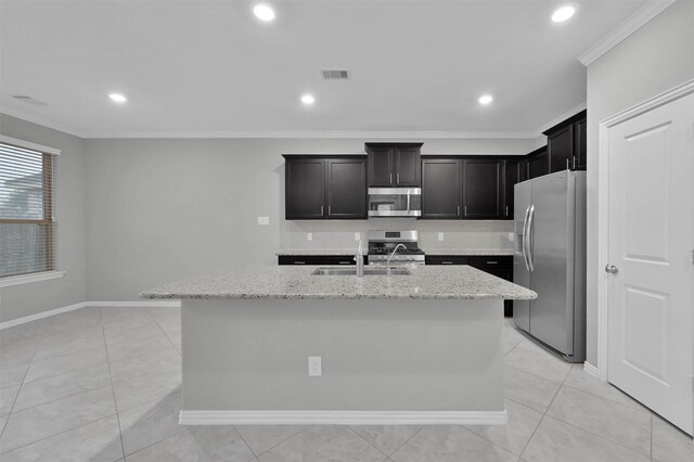 kitchen with sink, ornamental molding, appliances with stainless steel finishes, an island with sink, and light stone countertops