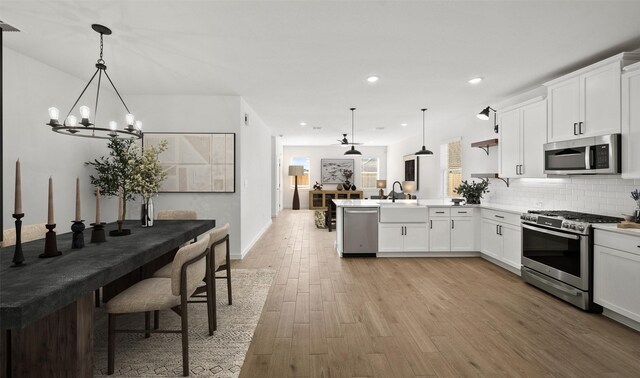 kitchen with pendant lighting, stainless steel appliances, white cabinets, and light wood-type flooring