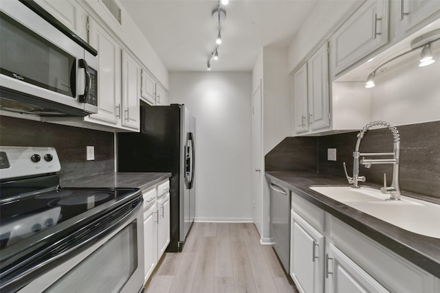 kitchen featuring tasteful backsplash, white cabinetry, sink, stainless steel appliances, and light hardwood / wood-style flooring