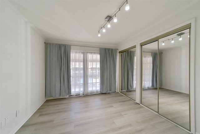 unfurnished bedroom with multiple closets, track lighting, and light hardwood / wood-style flooring