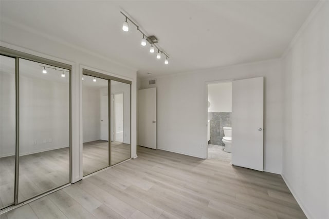 unfurnished bedroom with multiple closets, ensuite bathroom, rail lighting, and light hardwood / wood-style flooring