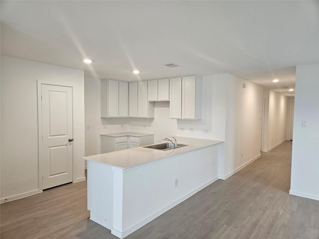 kitchen with sink, kitchen peninsula, white cabinets, and light hardwood / wood-style flooring