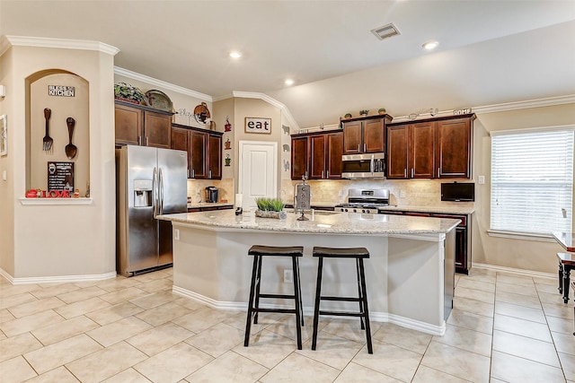 kitchen with light tile patterned floors, a breakfast bar area, appliances with stainless steel finishes, a kitchen island with sink, and light stone counters