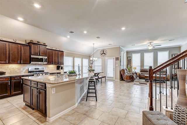 kitchen featuring light tile patterned flooring, decorative light fixtures, an island with sink, stainless steel appliances, and light stone countertops