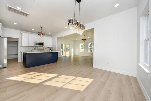 kitchen with light hardwood / wood-style flooring, appliances with stainless steel finishes, a kitchen island with sink, white cabinets, and decorative light fixtures