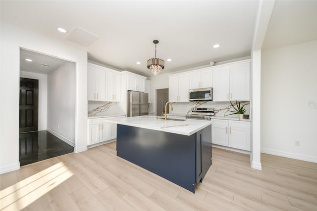 kitchen featuring sink, appliances with stainless steel finishes, white cabinetry, a kitchen island with sink, and decorative light fixtures