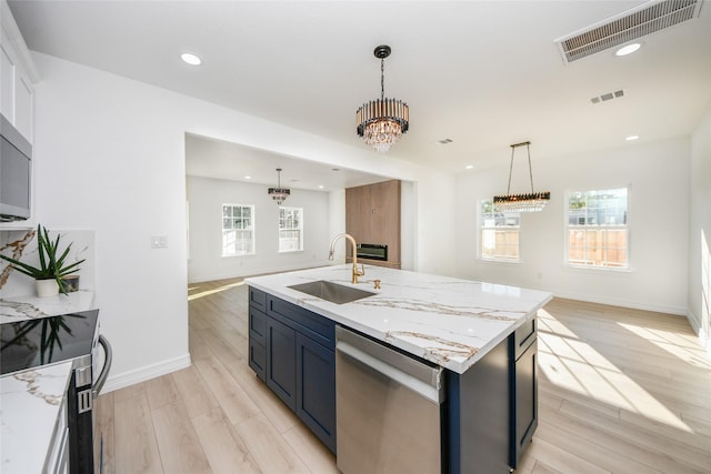 kitchen featuring sink, stainless steel appliances, hanging light fixtures, and a center island with sink