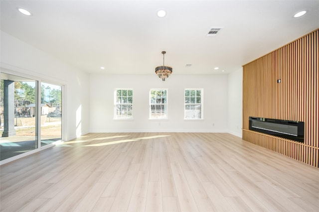 unfurnished living room featuring an inviting chandelier and light hardwood / wood-style floors