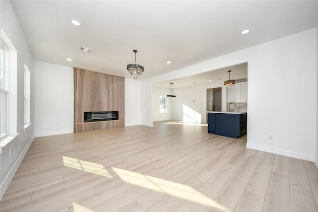 unfurnished living room featuring a large fireplace, light hardwood / wood-style floors, and a notable chandelier