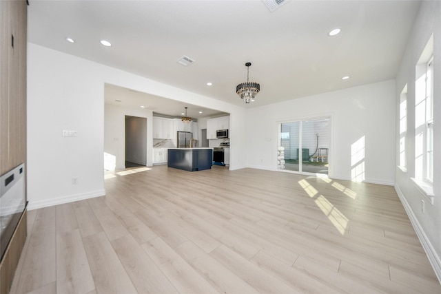 unfurnished living room featuring a notable chandelier, a wealth of natural light, and light hardwood / wood-style floors