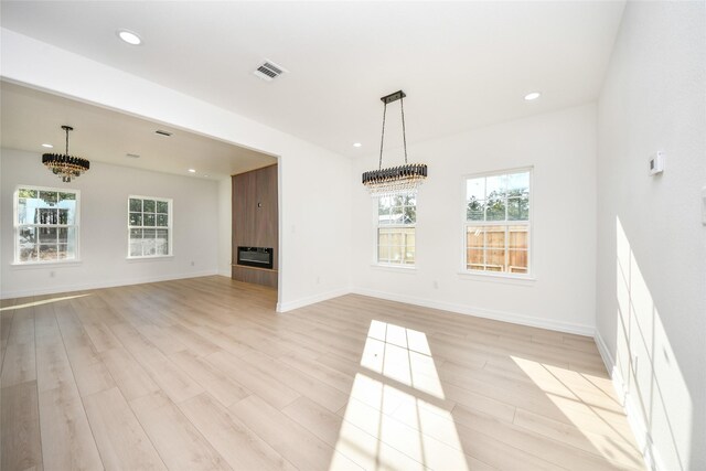 interior space with a tiled fireplace, heating unit, a notable chandelier, and light hardwood / wood-style flooring