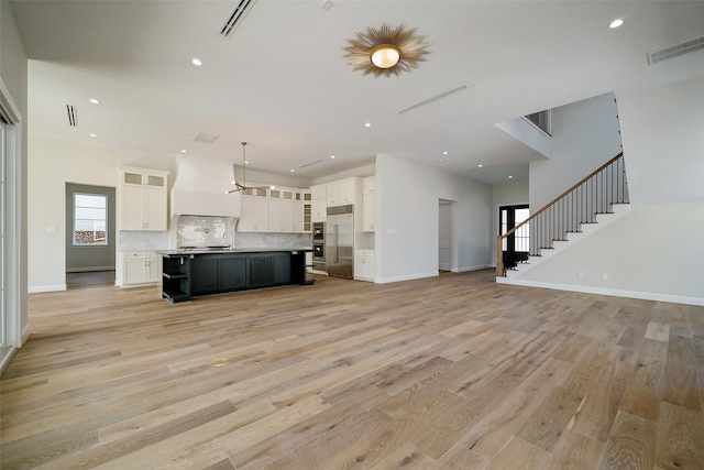 kitchen featuring a large island with sink, stainless steel built in refrigerator, custom range hood, and light wood-type flooring