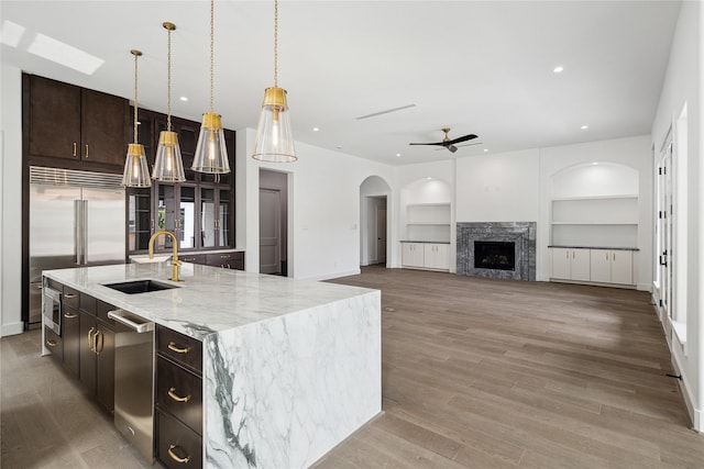 kitchen with sink, light wood-type flooring, built in features, stainless steel appliances, and a kitchen island with sink