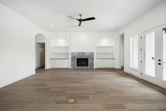 unfurnished living room with a high end fireplace, built in features, french doors, and light wood-type flooring