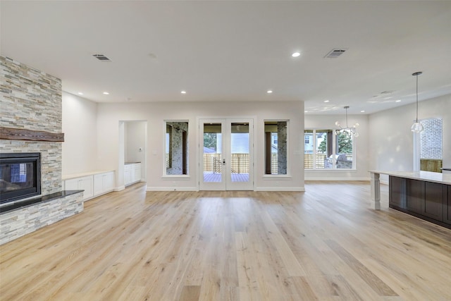 unfurnished living room featuring french doors, a chandelier, a fireplace, and light hardwood / wood-style floors