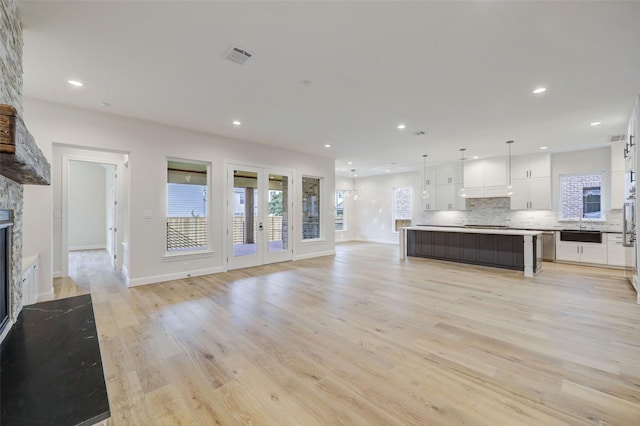 unfurnished living room with french doors, a stone fireplace, sink, and light hardwood / wood-style flooring