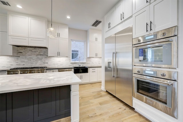 kitchen featuring sink, white cabinetry, stainless steel appliances, decorative light fixtures, and light wood-type flooring