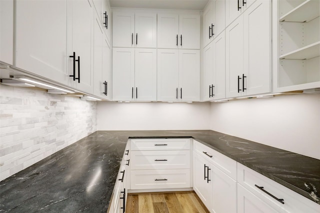 kitchen featuring decorative backsplash, white cabinets, light hardwood / wood-style floors, and dark stone counters