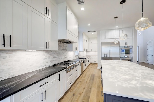 kitchen featuring appliances with stainless steel finishes, pendant lighting, white cabinets, decorative backsplash, and light hardwood / wood-style floors